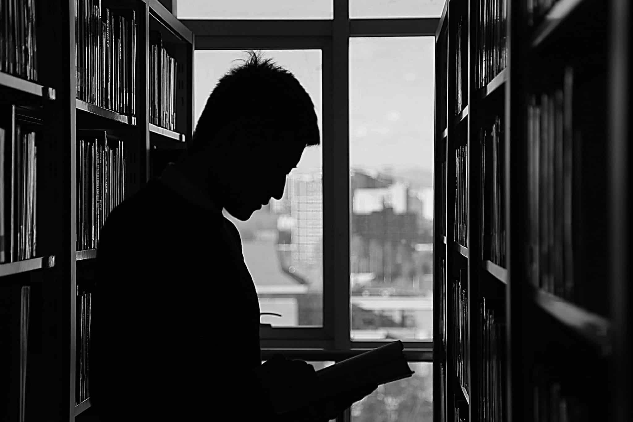 Ung mann i profil leser bok i biblioteket
